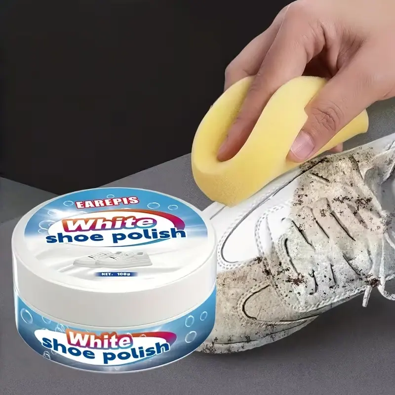Mano aplicando la crema limpiadora con la esponja sobre un tenis blanco sucio